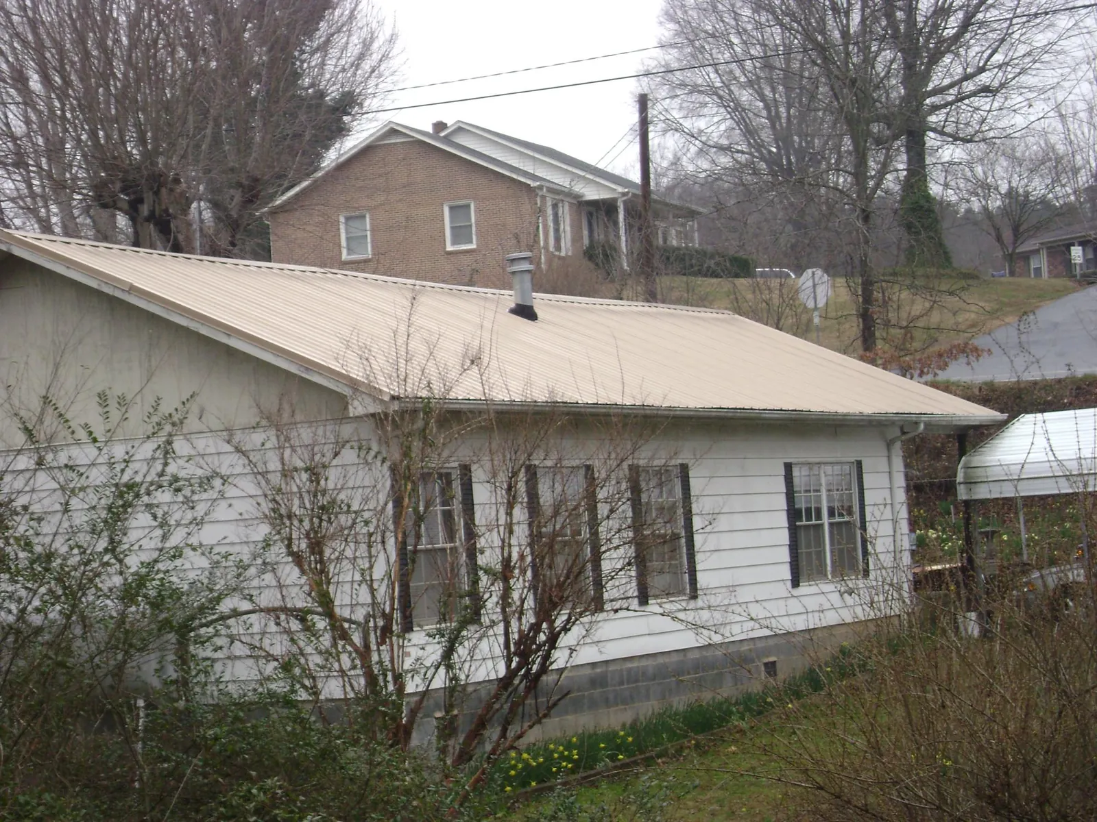 Tan metal roof on a white sided house set into a hillside — Commercial Roofing by Roofing Brothers in Garwood